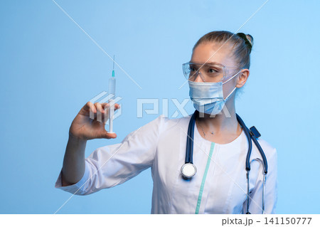 Doctor or nurse in medical mask and safety glasses holding a syringe with vaccine, preparing for injection Doctor or nurse in medical mask and safety glasses holding a syringe with vaccine, preparing for injection 141150777