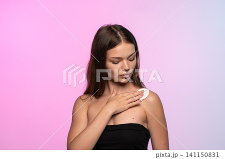 Young woman cleaning skin with a cosmetic cotton pad, performing daily hygiene and beauty routine Young woman cleaning skin with a cosmetic cotton pad, performing daily hygiene and beauty routine 141150831