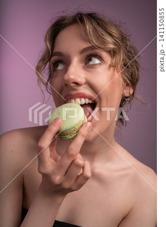 Young woman enjoying green french macaron, looking up with an eager expression on pink background Young woman enjoying green french macaron, looking up with an eager expression on pink background 141150855