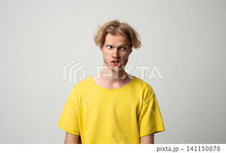 Young blonde man making funny face with skeptical and disgusted expression, showing disbelief and annoyance while looking aside Young blonde man making funny face with skeptical and disgusted expression, showing disbelief and annoyance while looking aside 141150878