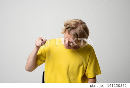 Blond man in yellow t-shirt pointing finger, laughing and mocking, showing disbelief or teasing on a plain studio background 141150882