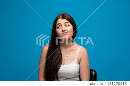 Young woman looking doubtful, showing hesitation, uncertainty, skepticism, and making a face on a blue background Young woman looking doubtful, showing hesitation, uncertainty, skepticism, and making a face on a blue background 141150918
