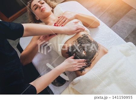 Beautiful woman in spa salon getting mud body massage Beautiful woman in spa salon getting mud body massage 141150955