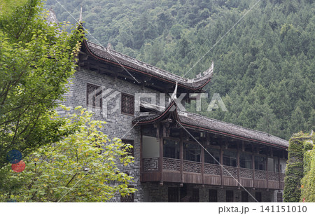 a traditional historic-style building at Chiyou Jiuli City cultural complex, featuring classic grey brick walls, an open wooden veranda, and elegant curved rooflines. Surrounded by lush green trees a traditional historic-style building at Chiyou Jiuli City cultural complex, featuring classic grey brick walls, an open wooden veranda, and elegant curved rooflines. Surrounded by lush green trees 141151010