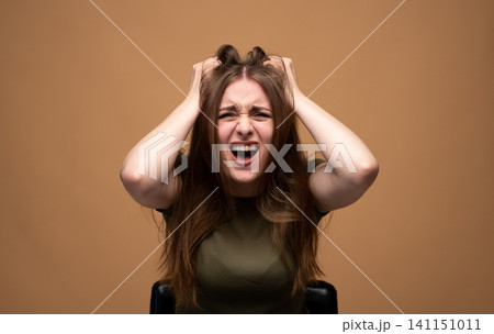 Young woman stressing out, screaming with hands clutching her hair, expressing frustration, anxiety, and extreme anger 141151011