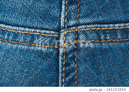 Blue denim fabric close up showing heavy stitching detail. Macro view of rugged jeans material with contrast thread. Textile background for fashion industry and clothing design concept Blue denim fabric close up showing heavy stitching detail. Macro view of rugged jeans material with contrast thread. Textile background for fashion industry and clothing design concept 141151054