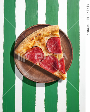 pizza slice on wooden plate on green and white striped painted background pizza slice on wooden plate on green and white striped painted background 141151315