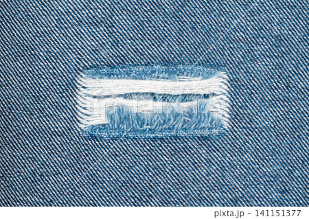 Torn denim fabric with frayed edges and exposed white threads Torn denim fabric with frayed edges and exposed white threads 141151377