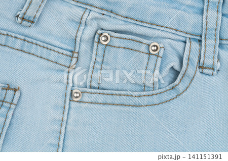 Light blue denim jeans coin pocket with metal rivets. Macro texture of casual clothing fabric. Close up detail of rugged pants material. Cotton textile design, fashion background Light blue denim jeans coin pocket with metal rivets. Macro texture of casual clothing fabric. Close up detail of rugged pants material. Cotton textile design, fashion background 141151391