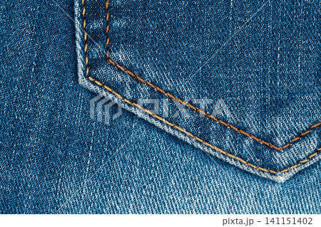 Closeup of blue denim fabric with orange stitching detail on pocket corner 141151402