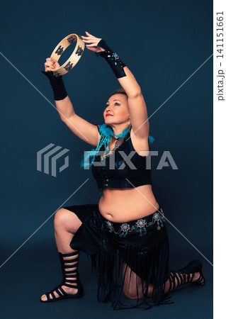 Woman stands on one knee and holds up tambourine and plays it Woman stands on one knee and holds up tambourine and plays it 141151661