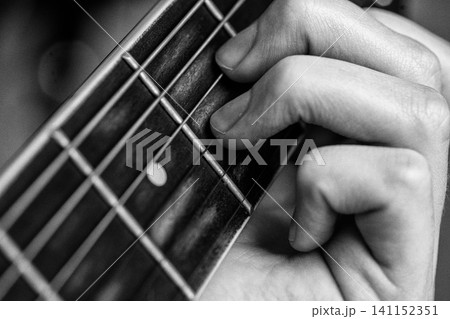Woman playing guitar. Closeup of hand on fretboard pressing string to play chord. Black and white Woman playing guitar. Closeup of hand on fretboard pressing string to play chord. Black and white 141152351
