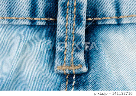 Blue jean belt loop detail closeup. Denim fabric texture with yellow stitching. Durable cotton clothing material and garment construction. Macro shot of blue pants for apparel design Blue jean belt loop detail closeup. Denim fabric texture with yellow stitching. Durable cotton clothing material and garment construction. Macro shot of blue pants for apparel design 141152716