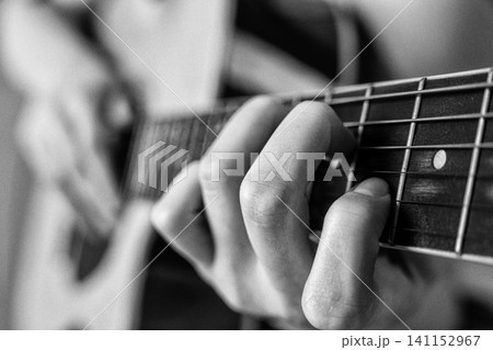 Woman playing guitar. Closeup of hand on fretboard. Monochrome photography with grain and soft focus Woman playing guitar. Closeup of hand on fretboard. Monochrome photography with grain and soft focus 141152967