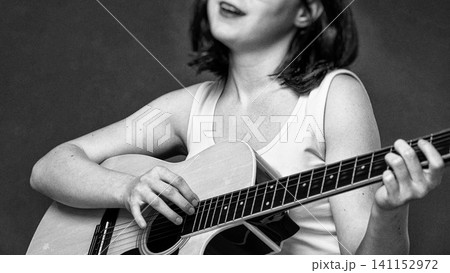 Young woman musician playing acoustic guitar, singing song with musical instrument. Black and white Young woman musician playing acoustic guitar, singing song with musical instrument. Black and white 141152972