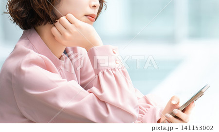 スマートフォンを持って考えごとをする女性・ビジネスウーマン 141153002