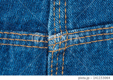 Denim texture with brown stitching detail, three needle job. Closeup of blue jeans fabric construction. Durable cotton material for clothing manufacture. Fashion industry background and textile design 141153064