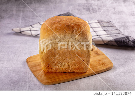 Freshly baked loaf of bread on wooden cutting board with checkered cloth 141153874