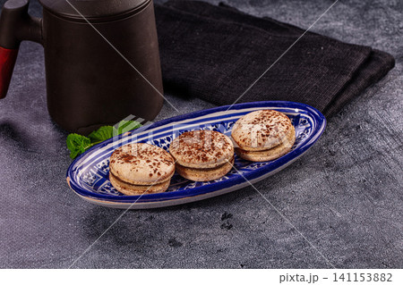 Three tiramisu macarons on blue ceramic plate with coffee pot Three tiramisu macarons on blue ceramic plate with coffee pot 141153882