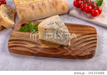 Slice of blue cheese on wooden cutting board with bread and tomatoes Slice of blue cheese on wooden cutting board with bread and tomatoes 141153888