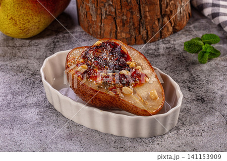 Baked pear half with honey glaze and pine nuts in ceramic dish Baked pear half with honey glaze and pine nuts in ceramic dish 141153909