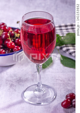 Red cherry juice in wine glass with fresh cherries and green leaves on light textured surface Red cherry juice in wine glass with fresh cherries and green leaves on light textured surface 141153932