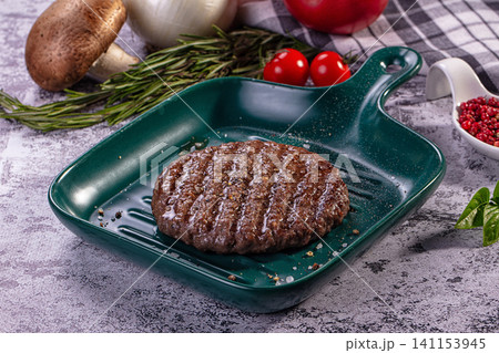 Grilled beef patty on green ceramic grill pan with fresh herbs and vegetables Grilled beef patty on green ceramic grill pan with fresh herbs and vegetables 141153945