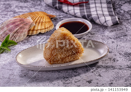 Triangular onigiri rice ball with soy sauce and seashells on rustic surface Triangular onigiri rice ball with soy sauce and seashells on rustic surface 141153949
