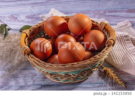 Brown eggs in woven basket on rustic wooden surface with wheat and cloth 141153950