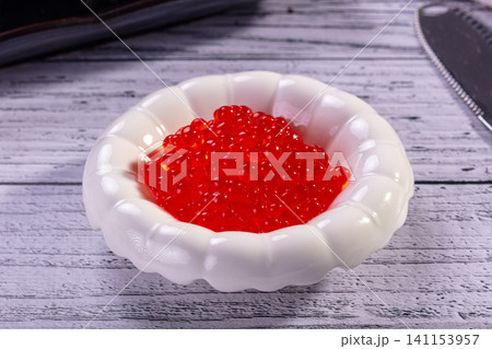 Red caviar in white ceramic bowl on rustic wooden table 141153957