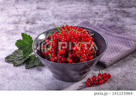 Fresh red currants in dark bowl with green leaves on textured gray surface 141153964