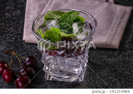 Cherry mint drink in textured glass with ice on dark surface Cherry mint drink in textured glass with ice on dark surface 141153969
