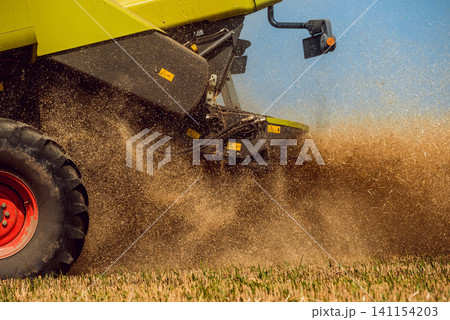 Combine harvester in action on wheat field. Process of gathering a ripe crop. Combine harvester in action on wheat field. Process of gathering a ripe crop. 141154203