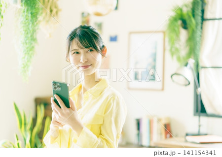 観葉植物に囲まれた部屋でスマホを操作する若い日本人女性 観葉植物に囲まれた部屋でスマホを操作する若い日本人女性 141154341
