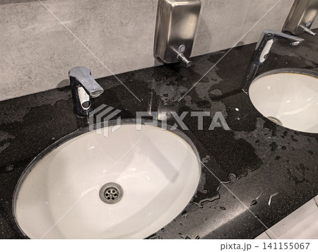 Wet black granite countertop with white sinks and chrome faucets closeup Wet black granite countertop with white sinks and chrome faucets closeup 141155067
