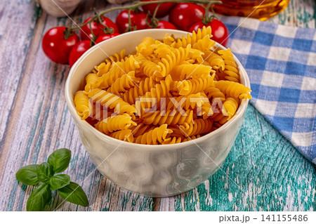 Fusilli pasta in ceramic bowl with cherry tomatoes basil and checkered cloth on rustic wood 141155486