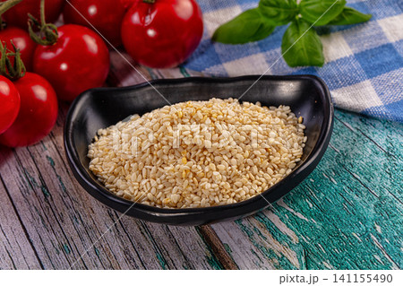 Sesame seeds in black bowl with cherry tomatoes and basil on rustic wooden table Sesame seeds in black bowl with cherry tomatoes and basil on rustic wooden table 141155490