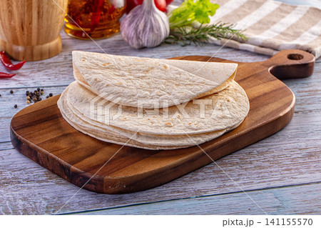 Stack of fresh tortillas on a wooden cutting board with garlic and herbs Stack of fresh tortillas on a wooden cutting board with garlic and herbs 141155570