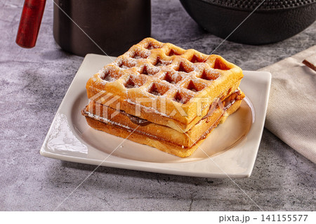 A stack of golden Belgian waffles filled with chocolate spread and dusted with powdered sugar on a white plate 141155577