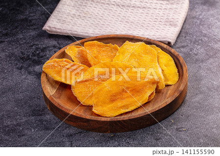 Dried mango slices on wooden plate with textured cloth background Dried mango slices on wooden plate with textured cloth background 141155590