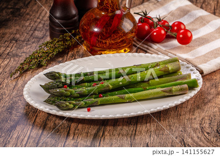 Fresh green asparagus spears on white plate with cherry tomatoes and oil bottle on rustic wood table Fresh green asparagus spears on white plate with cherry tomatoes and oil bottle on rustic wood table 141155627