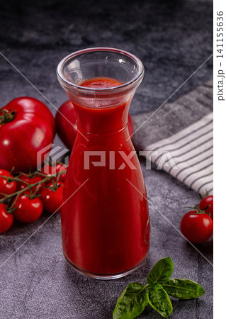 Glass carafe filled with vibrant red tomato juice surrounded by fresh tomatoes and basil on dark textured surface Glass carafe filled with vibrant red tomato juice surrounded by fresh tomatoes and basil on dark textured surface 141155636