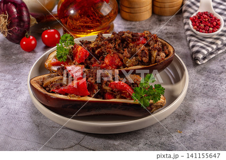 Stuffed eggplant halves with ground meat and red peppers on rustic plate 141155647