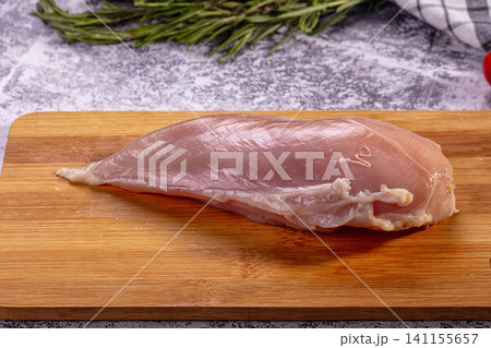 Raw chicken breast on wooden cutting board with rosemary and kitchen towel Raw chicken breast on wooden cutting board with rosemary and kitchen towel 141155657