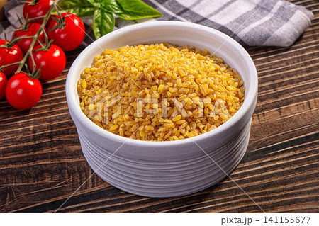 Bulgur wheat in white ceramic bowl with cherry tomatoes and basil on wooden table Bulgur wheat in white ceramic bowl with cherry tomatoes and basil on wooden table 141155677