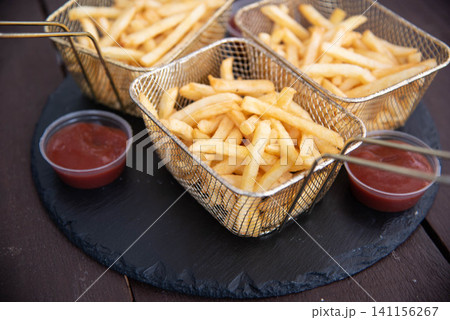Beautiful serving of French fries with ketchup. French fries in a serving basket with sauce on a stone platter. Beautiful serving of French fries with ketchup. French fries in a serving basket with sauce on a stone platter. 141156267