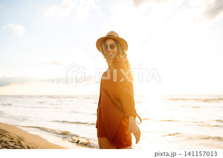 Carefree woman tourist walking along ocean sandy beach at sunset. Travel, weekend, lifestyle concept Carefree woman tourist walking along ocean sandy beach at sunset. Travel, weekend, lifestyle concept 141157013