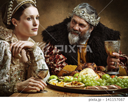 King, queen and talk with feast at table for fine dinning in royal banquet, vintage and majestic with crown. Monarch, husband and bored together with alcohol for buffet for formal celebration. 141157087