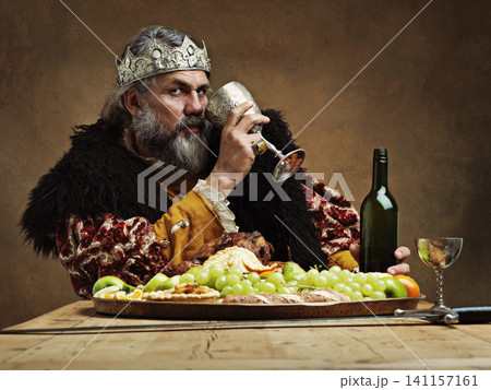 King, confident and feast at table with wine glass as royalty in studio on brown background for tradition, culture and meal. Portrait, monarch and leader with eating buffet or supper with confidence King, confident and feast at table with wine glass as royalty in studio on brown background for tradition, culture and meal. Portrait, monarch and leader with eating buffet or supper with confidence 141157161