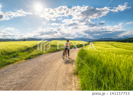 Woman riding mountain bike on dirt road and green wheat fields 141157753